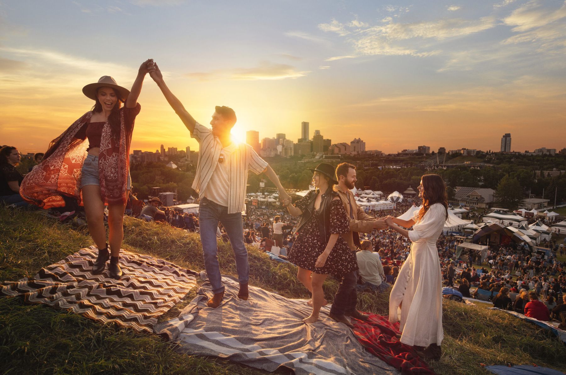 Friends dancing at sunset above the Edmonton Folk Music Festival, with the downtown skyline behind them